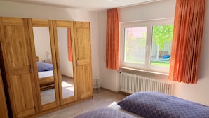 A bedroom with a wooden wardrobe, a bed with two pillows, a window with curtains, and a radiator. - Bright apartment (ground floor) with garden and terrace. Experience Hegau, Lake Constance, Rhine Falls! (Tengen)