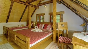 A wooden bedroom with a sloped ceiling, a double bed, a chair, and a small table with a vase of flowers. - Sobol in Kočičin (Haus für 6-9 Personen) (Kuzelj)