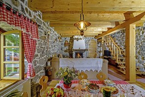 Une pièce rustique aux murs de pierre, avec des poutres apparentes, une cheminée, une table à manger dressée et un escalier.