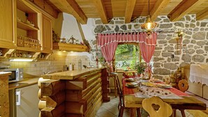 A rustic kitchen with wooden cabinets, a stone wall, and a dining area with a checkered tablecloth. - Sobol in Kočičin (Haus für 6-9 Personen) (Kuzelj)