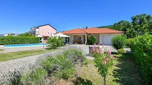 Ein zweistöckiges Haus mit Swimmingpool, umgeben von viel Grün und blauem Himmel.