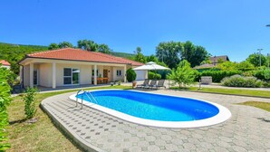 Ein Wohnhaus mit Schwimmbad, einer überdachten Terrasse und einem Garten.