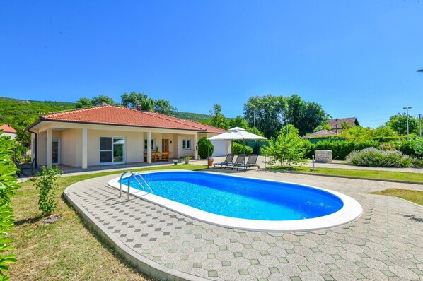 Una propiedad residencial con piscina, terraza techada y jardín.