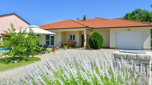 Ein zweistöckiges Haus mit rotem Ziegeldach, einer überdachten Veranda mit Gartenmöbeln und einem Garten mit weißen Blumen.