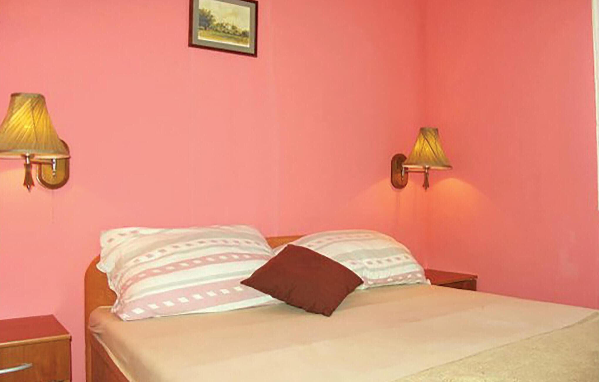 A bedroom with pink walls, two bedside lamps, a bed with patterned pillows, and a small bedside table.