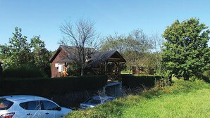 Entorno rural con una estructura de madera, posiblemente un granero o cobertizo, rodeado de vegetación y un cielo despejado.