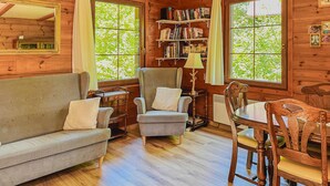 A cozy cabin interior with a sofa, armchair, wooden dining table, and a bookshelf filled with books. - 3 bedroom lovely home in Nowe Warpno (Nowe Warpno)
