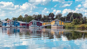 Une rangée de maisons flottantes aux couleurs vives, reliées par un pont, et situées au-dessus d’une étendue d’eau calme.