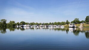 Un port de plaisance où plusieurs bateaux sont amarrés le long du quai, entouré d’arbres et sous un ciel dégagé.
