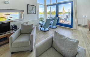 Un salon moderne avec une grande fenêtre donnant sur un lac, des canapés gris, un téléviseur et un tableau encadré accroché au mur.