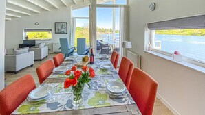 Un coin repas avec une longue table dressée pour six personnes, agrémenté d’une nappe à motifs floraux, de chaises rouges et d’un vase contenant des roses rouges.