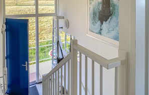 A staircase with a white railing leading to a balcony. A blue door is visible on the left, and a painting of a lighthouse is on the wall to the right.