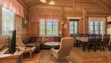 L’intérieur d’un chalet accueillant, avec des murs en bois, un canapé, une table à manger et un téléviseur.