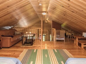 A cozy attic room with a wooden ceiling, a leather sofa, a coffee table, and a crib.