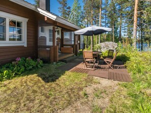 A wooden deck with a table and chairs, a covered outdoor area, and a stone feature.