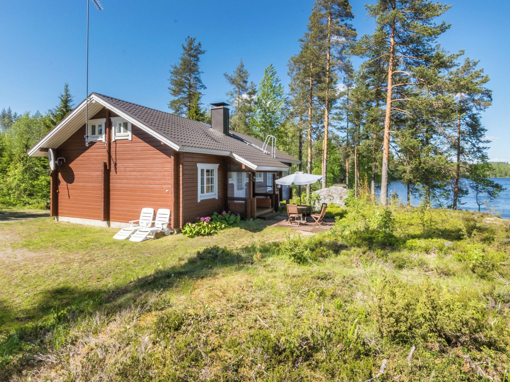 A wooden cabin with a deck, surrounded by trees and a lake.