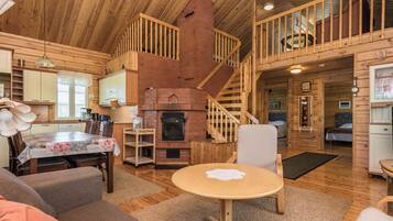 Un intérieur de chalet chaleureux comprenant un coin repas, une cuisine, une cheminée et un escalier menant à un étage supérieur.