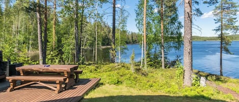 A wooden picnic table on a deck with a lake and forest in the background.