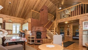 A log cabin interior with a fireplace, wooden staircase, and a dining area.