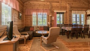 A cozy cabin interior with a sofa, armchairs, a dining table, and a television.