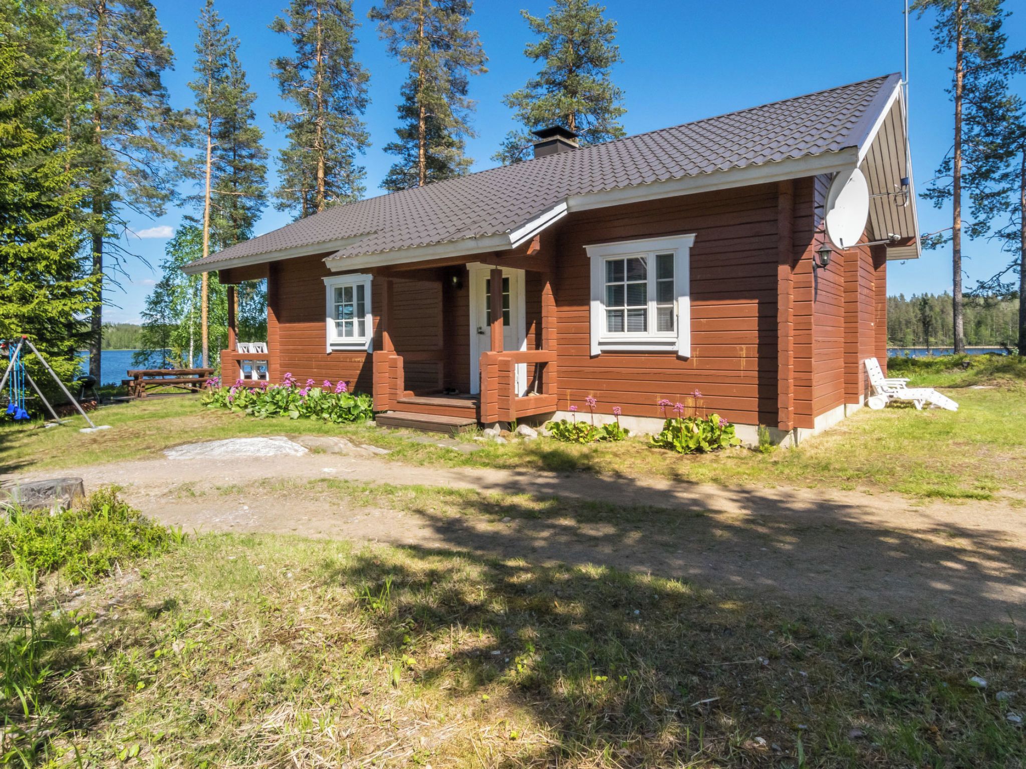 A wooden cabin with a porch, a small deck, and a view of a lake.