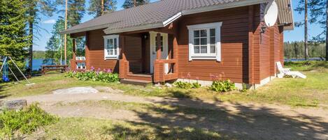 A wooden cabin with a porch, a small deck, and a view of a lake.