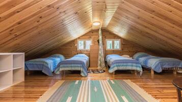 Une chambre mansardée chaleureuse avec des lambris en bois au plafond, un lit central et deux petits lits de chaque côté.