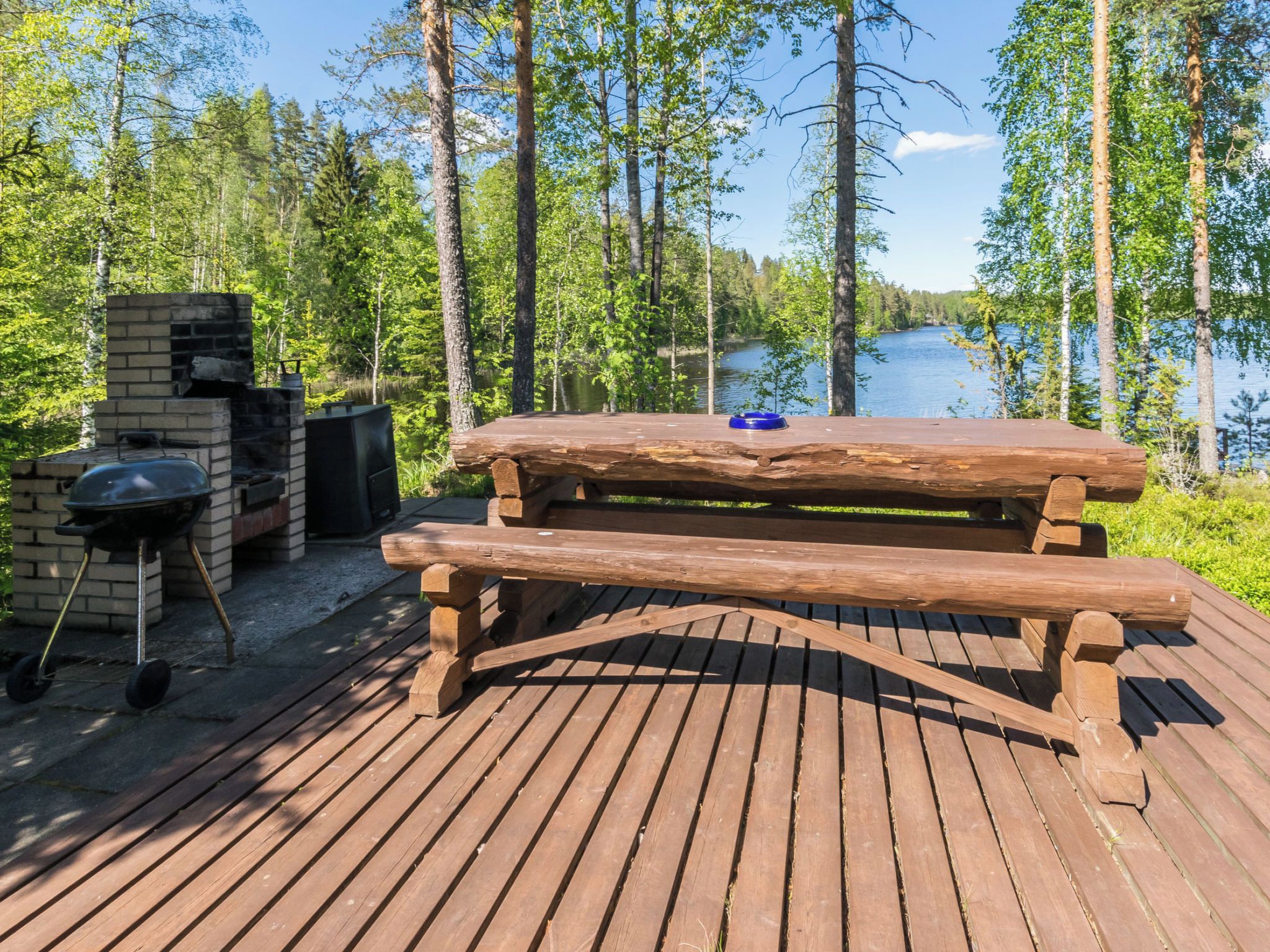A wooden deck with a picnic table and barbecue grill overlooking a lake.