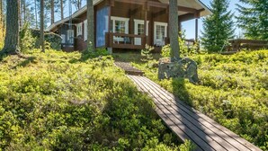 A wooden cabin with a deck, surrounded by dense forest and tall trees.