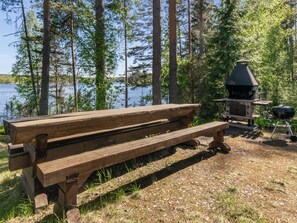 A wooden picnic table with a grill and a water body in the background. - Lehtimaja by Interhome (Parikkala)