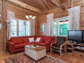 A cozy living room with wooden walls, a red sofa, a brown armchair, a coffee table, and a television. - Lehtimaja by Interhome (Parikkala)