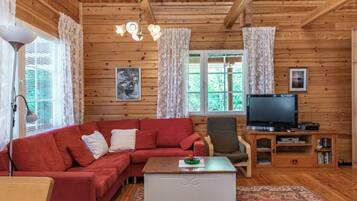 Un salon chaleureux avec un canapé rouge, une table basse, un téléviseur et des murs en bois.