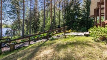 Une terrasse en bois avec un escalier menant à un bâtiment, le tout entouré d’arbres et bordé par une étendue d’eau.