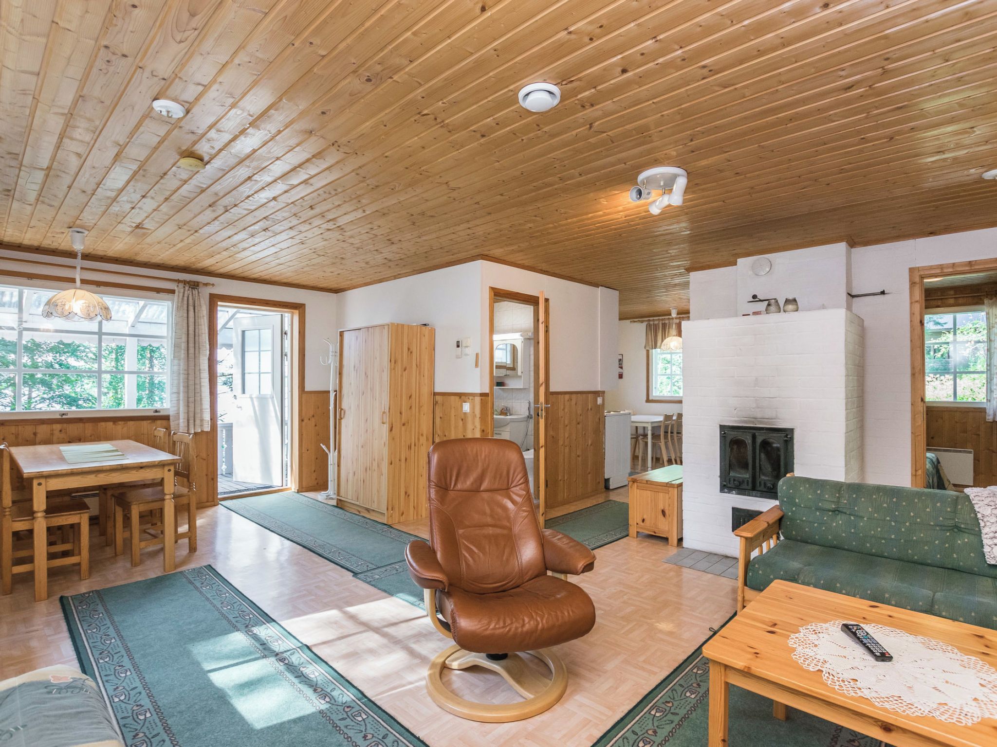 A wooden interior with a dining area, a leather chair, a sofa, and a fireplace.