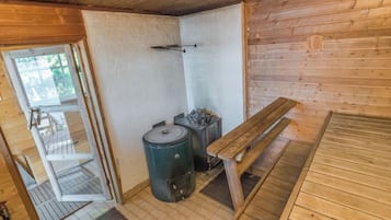 Interno di una baita in legno con una panca, un tavolo, un fornello e una porta che dà sull'esterno.