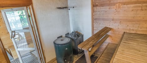 A wooden cabin interior with a bench, a table, a stove, and a door leading outside.