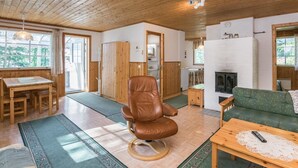 A cozy cabin interior with a wooden ceiling, a dining area with a table and chairs, a leather armchair, a green sofa, and a fireplace. - Kiviaho by Interhome (Parikkala)