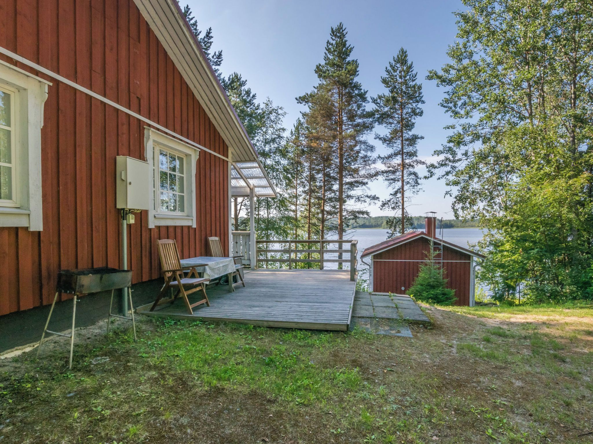 Puisesta laudasta rakennettu terassi, jossa on pöytä ja tuoleja, pieni varasto ja punainen rakennus, jossa on ikkuna.