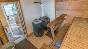 A sauna room with wooden benches, a sauna heater, and a small table. - Kiviaho by Interhome (Parikkala)