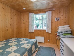 A wooden cabin room with a bed, a window with curtains, a radiator, and a stack of pillows. - Kiviaho by Interhome (Parikkala)