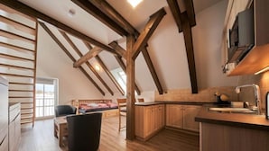 A loft-style bedroom with a sloped ceiling and exposed wooden beams, a small kitchenette with wooden cabinets, and a view through a large window. - Na Pomezkách by Interhome (Malá Úpa)