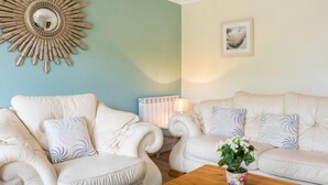Een kamer met twee crèmekleurige banken, een houten salontafel, een decoratieve zonnespiegel, een radiator en een lijst met een foto aan de muur.