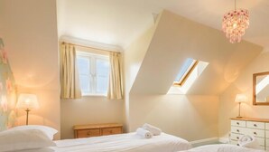 Een slaapkamer met twee bedden, een dakraam, een dressoir en een lamp.