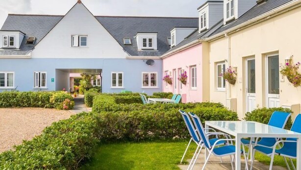 A residential building with a central entrance, a covered patio, and a small garden area with a table and chairs. - Beautiful 4* Self-Catering, by Stunning Cliffs & Bays - Three Bedroom Cottage (Guernsey)