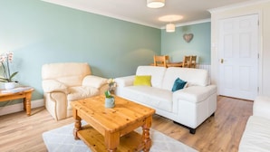 A living room with a beige sofa, a white sofa, a wooden coffee table, and a small table with a plant. - Beautiful 4* Self-Catering, by Stunning Cliffs & Bays - Three Bedroom Cottage (Guernsey)