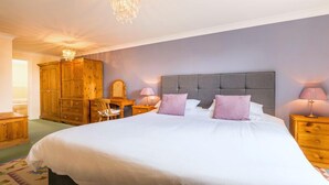 A bedroom with a large bed, wooden wardrobe, and a chandelier. - Beautiful 4* Self-Catering, by Stunning Cliffs & Bays - Three Bedroom Cottage (Guernsey)