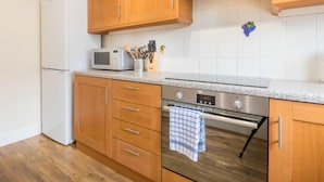 A kitchen with wooden cabinets, a microwave, a stainless steel oven, and a tiled backsplash. - Beautiful 4* Self-Catering, by Stunning Cliffs & Bays - Three Bedroom Cottage (Guernsey)