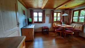 Ein gemütliches Blockhauszimmer mit Holzböden, einem Esstisch mit Stühlen, einem kleinen Schreibtisch mit Computer und einem Fenster mit Vorhängen.