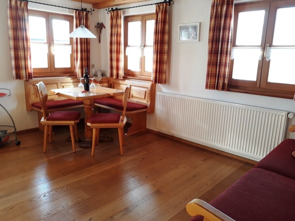 A dining area with a wooden table and chairs, a radiator, and plaid curtains.