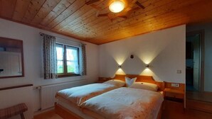 Ein Schlafzimmer mit zwei Betten, Holzbalkendecke, einem fenster mit Vorhängen und Wandleuchten.